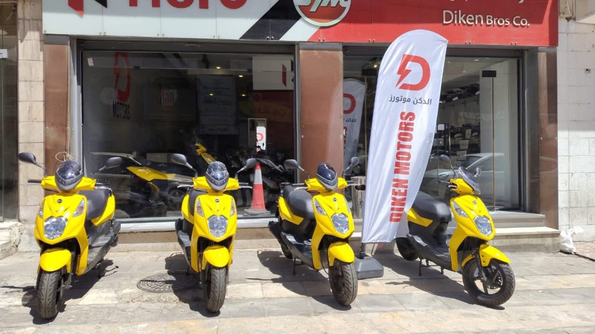 Diken Motors showroom in Amman with Hero and SYM signage and a row of new scooters out front