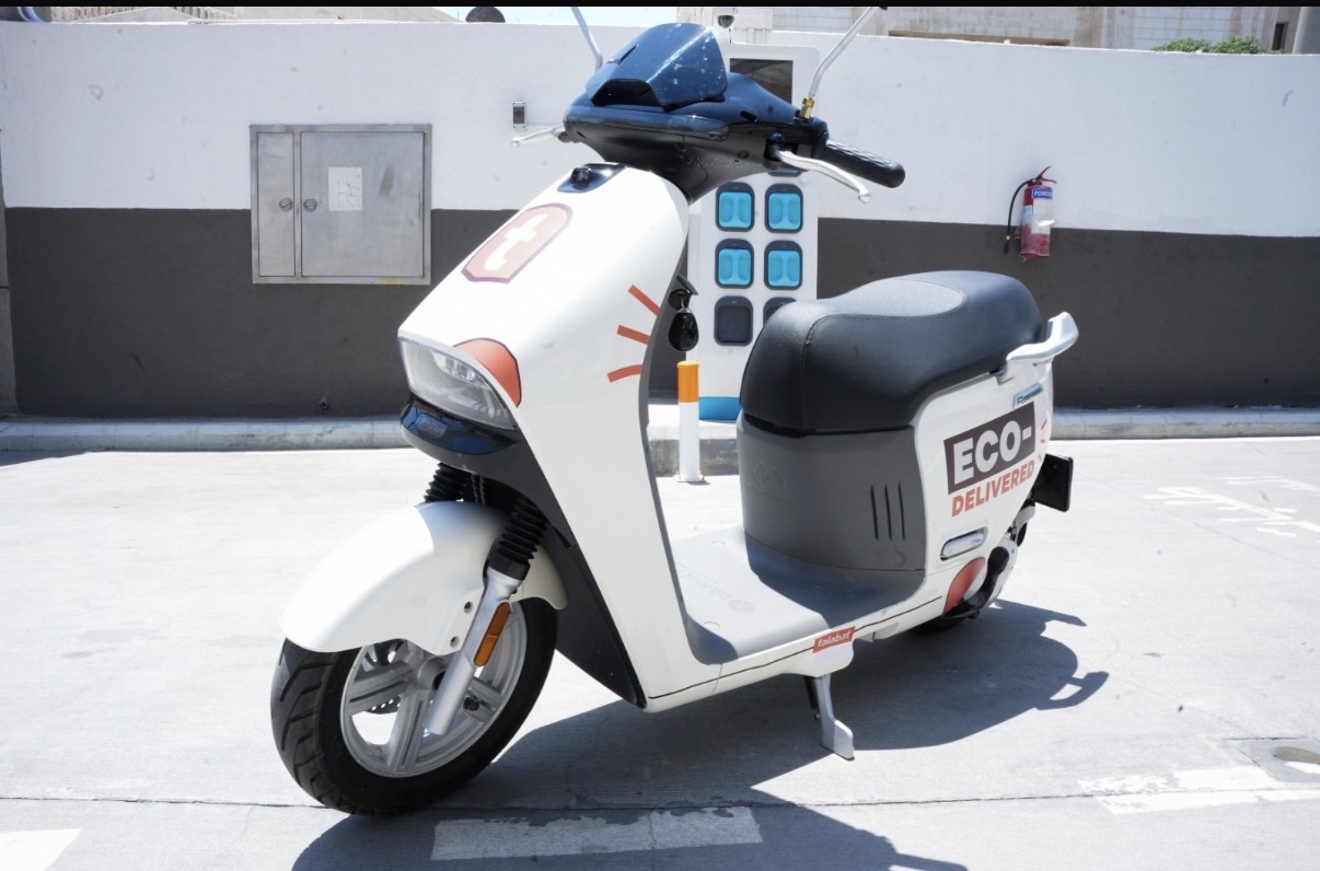 Blue Shark electric scooter in Talabat livery beside a battery-swap cabinet